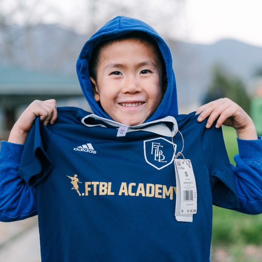 Smiling youth player holding up his FTBL Academy jersey.